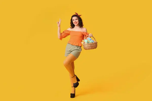 Schöne Pin Frau Mit Osterkorb Zeigt Siegesgeste Auf Gelbem Hintergrund — Stockfoto