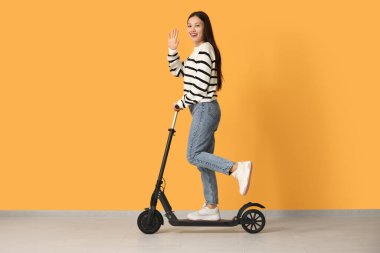 Güzel genç Asyalı kadın sarı duvarın yanında modern elektrikli scooter kullanıyor.