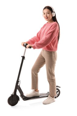 Beyaz arka planda modern elektrikli scooterlı kulaklıklı güzel bir Asyalı kadın.