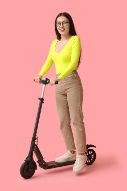 Pembe arka planda modern elektrikli scooterı olan mutlu genç Asyalı kadın.