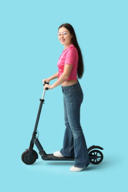 Mavi arka planda modern elektrikli scooterlı güzel bir Asyalı kadın.