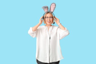 Mavi arka planda kulaklığı olan, tavşan kulaklı mutlu yetişkin kadın operatör. Paskalya kutlaması