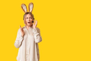 Sarı arka planda kulaklıklı, tavşan kulaklı, yetişkin bir kadın operatör. Paskalya kutlaması