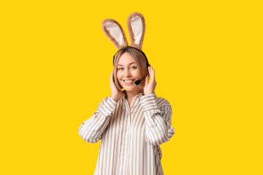 Sarı arka planda kulaklığı olan, tavşan kulaklı mutlu yetişkin kadın operatör. Paskalya kutlaması