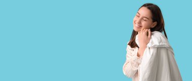 Pijamalı ve mavi arka planda battaniyesi olan mutlu genç bir kadın.