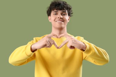 Yakışıklı genç adam, elleri yeşil arka planda kalp yapıyor.