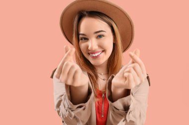 Pembe arka planda parmaklarıyla kalp yapan genç kadın, yakın plan.