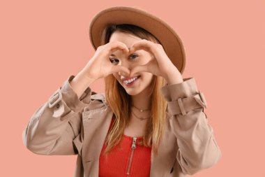 Elleri pembe arka planda kalp yapan genç bir kadın.