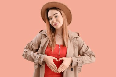 Elleri pembe arka planda kalp yapan genç bir kadın.