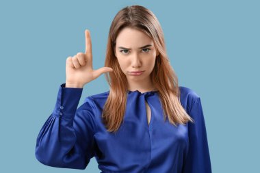 Upset young woman showing loser gesture on blue background clipart