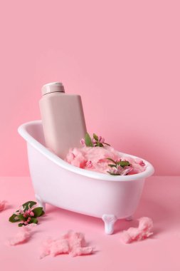 Duvar kenarındaki küçük küvetli kompozisyon, bir şişe şampuan ve pamuk.