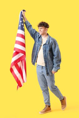 Sarı arka planda ABD bayrağı taşıyan genç adam.