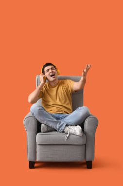 Kulaklıklı genç adam kırmızı arka planda koltukta müzik dinliyor.