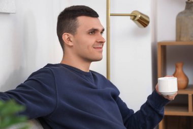 Modern oturma odasındaki kanepede oturan bir fincan kahveyle yakışıklı genç adam.