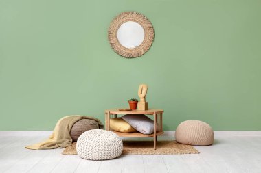 Yeşil duvarın yanında yastıklar ve puflar olan kahve masası.