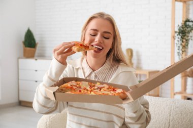 Evde lezzetli pizza yiyen genç bir kadın.