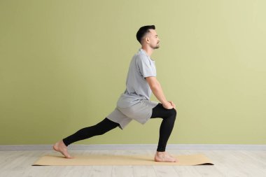 Yakışıklı adam yeşil duvarın yanında yoga yapıyor.