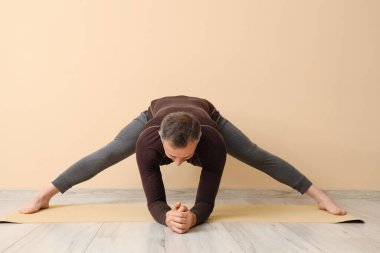 Olgun bir adam bej duvarın yanında yoga yapıyor.