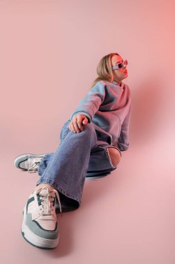 Kotlu, güneş gözlüklü, açık arka planda oturan hoş bir genç kadın.