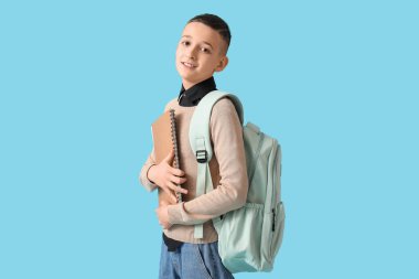 Sırt çantası ve mavi arka planda not defteri olan tatlı bir okul çocuğu.