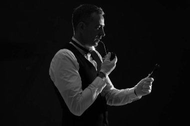 Büyüteci olan ve siyah arka planda sigara içen olgun dedektif silueti.