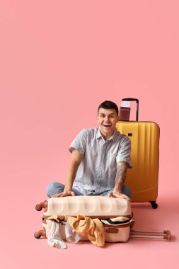 Pembe arka planda bavul dolusu elbisesi olan genç bir turist.