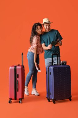 Turuncu arka planda bavulları ve pasaportları olan iki turist.