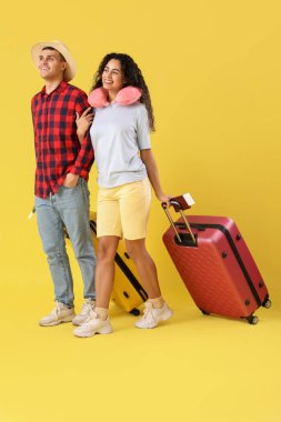 Çantalı ve pasaportlu bir çift turist sarı arka planda yürüyor.