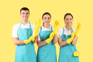 Sarı arka planda lastik eldivenli temizlik işçileri.