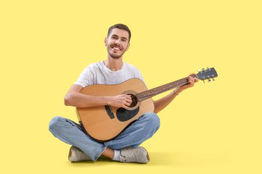 Sarı arka planda gitar çalan yakışıklı genç adam.