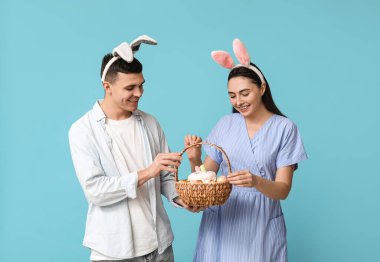 Mavi arka planda Paskalya tavşanı kulakları ve sepeti olan mutlu genç çift.