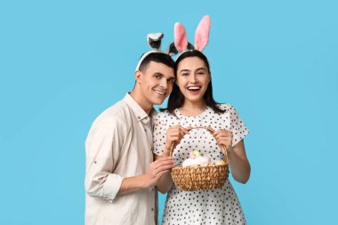 Paskalya sepeti ve mavi arka planda tavşan kulaklı mutlu genç çift.