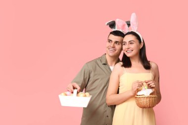 Paskalya sepetleri ve pembe arka planda tavşan kulakları olan mutlu genç çift.