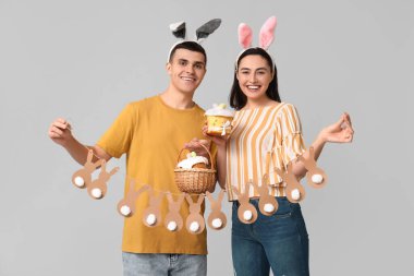 Paskalya pastası, çelenk ve gri arka planda tavşan kulaklı mutlu genç çift.