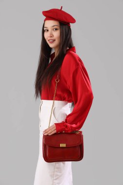 Gri arka planda şık bir çantası olan güzel, mutlu, Asyalı bir kadın.