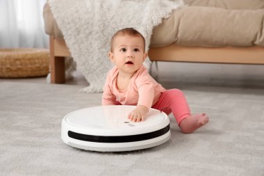 Evdeki halının üzerinde robot süpürgesi olan şirin bir bebek.