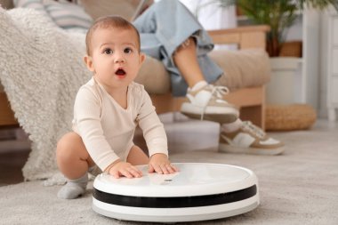 Robot elektrikli süpürgeyle küçük şirin bir bebek ve annesi evdeki kanepede oturuyor.