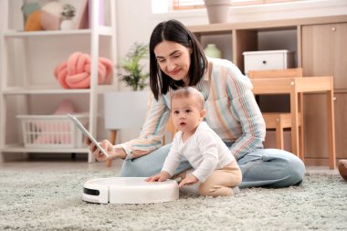 Robot elektrikli süpürgesi olan sevimli bir bebek ve evde tablet bilgisayar kullanan bir anne.