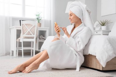 Yatak odasında cep telefonu kullanan duştan sonra havlusu olan genç bir kadın.