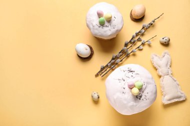 Paskalya pastaları, oyuncak tavşancık, söğüt dalları ve bej arka planda boyanmış yumurtalar.