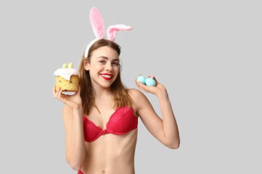 Paskalya pastası ve beyaz arka planda yumurtaları olan tavşan kulaklı seksi bir genç kadın.