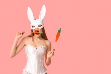 Pembe arka planda kağıt havuçlu tavşan maskeli seksi genç kadın. Paskalya kutlaması