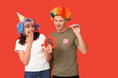 Parti düdüğü ve kırmızı arka planda osuruk yastığı olan komik kılık değiştirmiş genç arkadaşlar. 1 Nisan kutlamaları