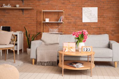 Çağdaş oturma odasının içinde çiçekler, hediye kutusu ve oturma odasındaki sehpanın üstünde takvim.