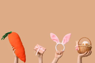 Paskalya sepeti, hediye kutusu, oyuncak havuç ve bej arka planda tavşan kulağı olan kadın elleri.
