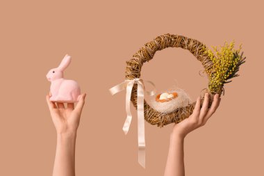 Paskalya çelengi ve bej arka planda tavşan tutan kadın elleri.