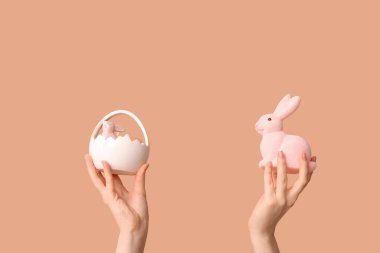 Paskalya sepetinde bej arka planda tavşan tutan kadın eller.