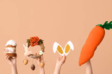 Paskalya pastası, çelenk, tavşan kulağı ve bej arka planda oyuncak havuç tutan kadın elleri.