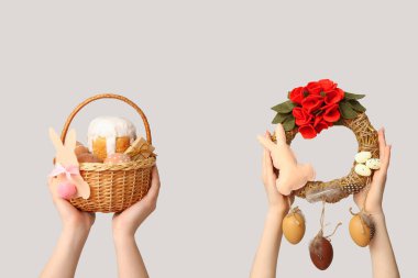 Beyaz arka planda Paskalya yumurtası ve çelengi olan kadın eller sepeti tutuyor.