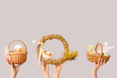 Beyaz arka planda Paskalya yumurtası ve çelenk bulunan sepetleri tutan kadın eller.